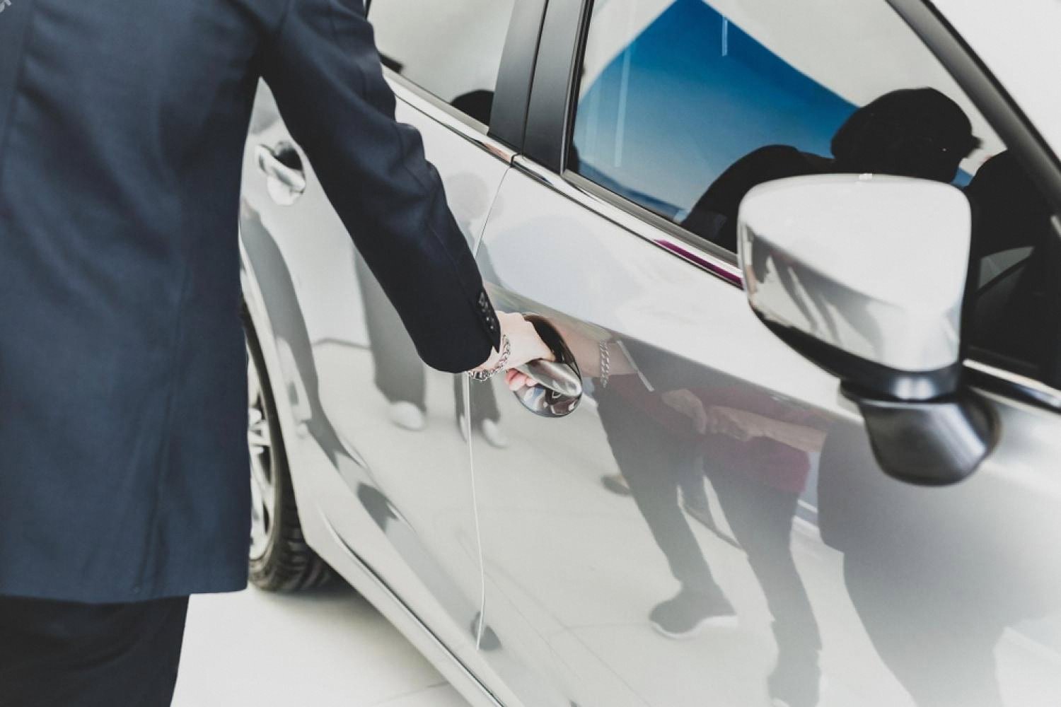 Dealer opening the door of a silver family sedan for a customer